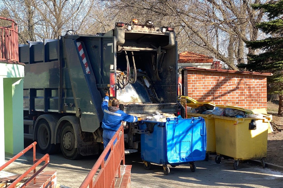 Worker loading a bin of debris into the back of a hauling truck
